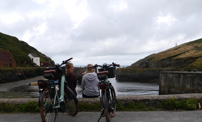 Two women sat at harbour with their e-bikes behind them.